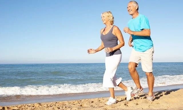 Senior Couple In Fitness Clothing Running Along Beach